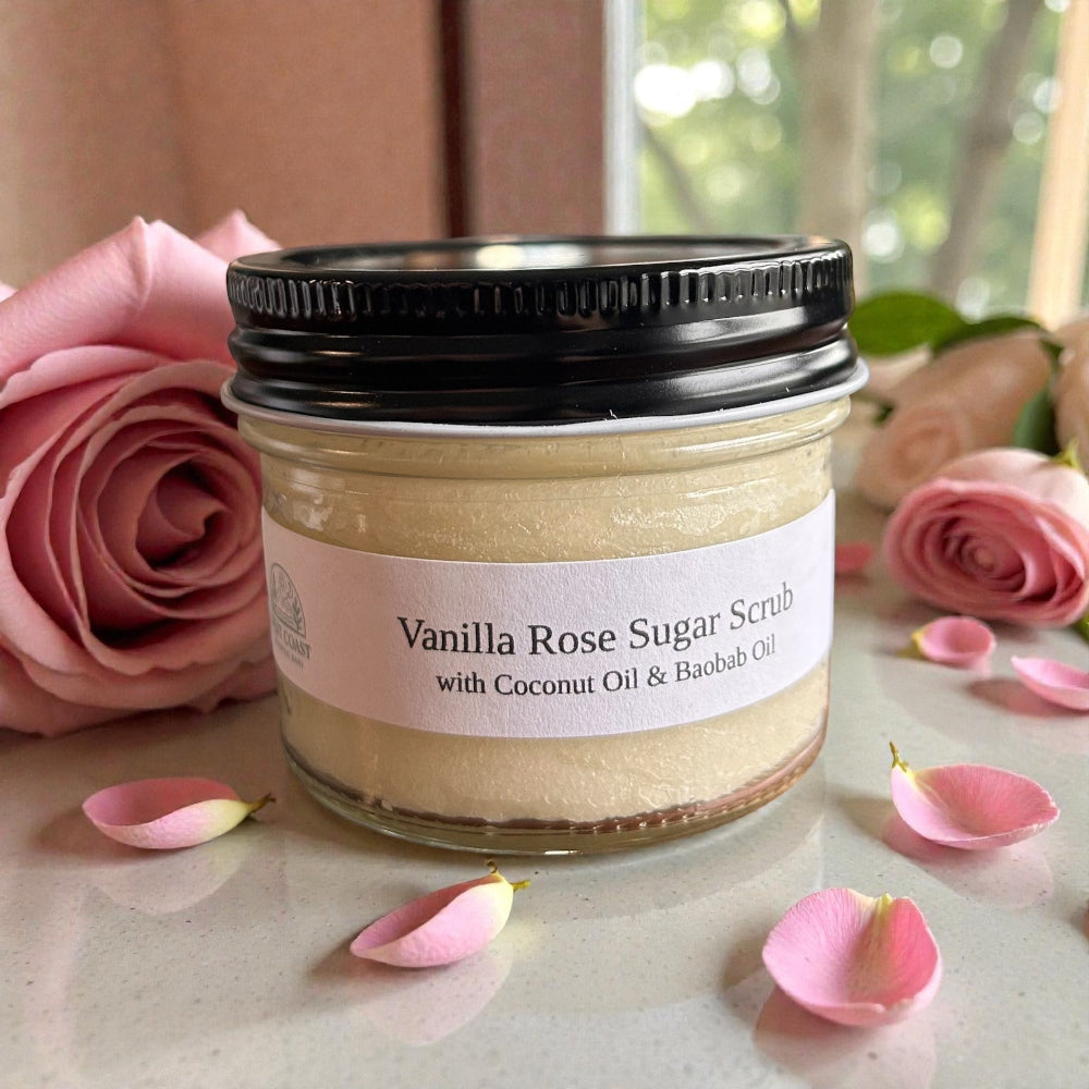 Jar of Vanilla Rose Sugar Scrub with coconut oil and baobab oil on a surface with pink roses and petals.